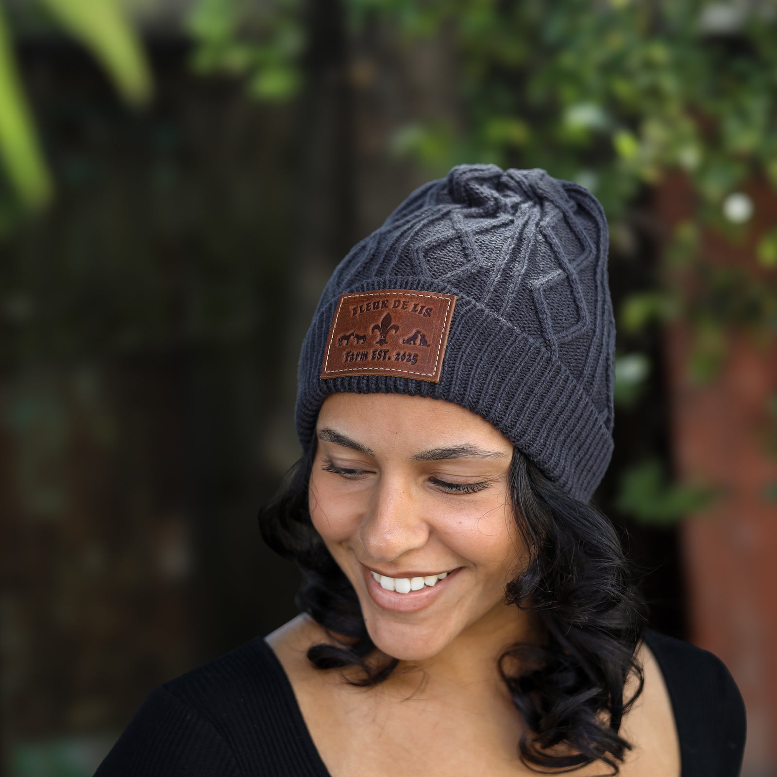 A woman wearing a dark gray cable-knit beanie with a brown leather patch that reads 'Tibet Peak Gear Co. Inc.